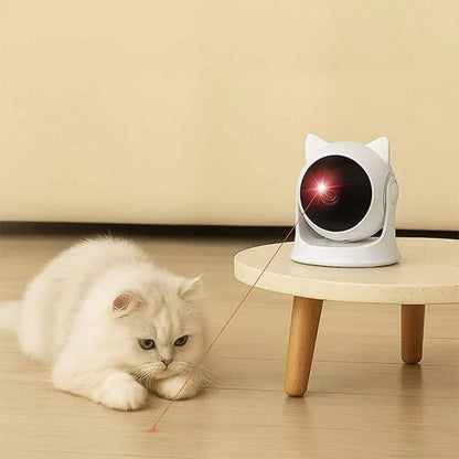 Jouet interactif blanc projetant un faisceau rouge près du chat blanc au sol.