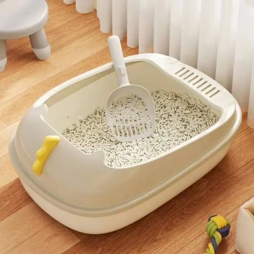 Bac à litière pour chat beige/blanc, intérieur avec grille et litière, pelle jaune visible.