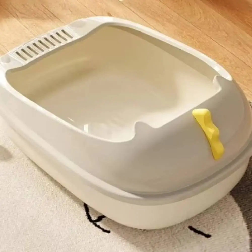 Bac à litière pour chat beige/blanc avec pelle jaune sur le rebord et grille ventilée.