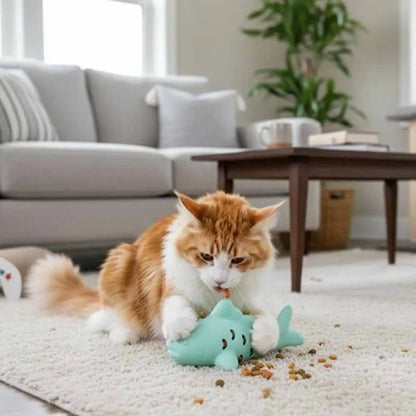 Jeu pour chat en forme de poisson turquoise, sur tapis, avec un chat assis.