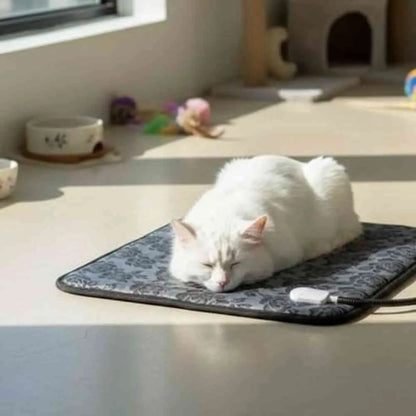 Tapis chauffant pour chat gris foncé à motif, bord noir, chat blanc roulé en boule.