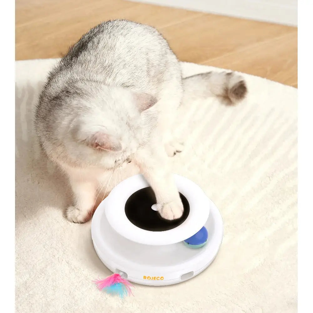 Jouet interactif pour chat : socle blanc avec bouton noir et plume multicolore.
