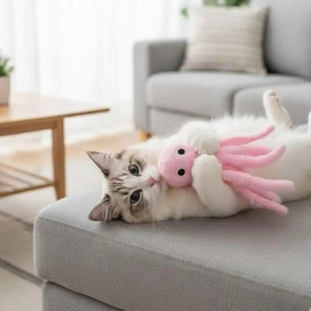 Peluche pieuvre interactive rose, posée sur un canapé avec deux chatons
