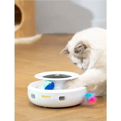 Jouet interactif pour chat ROJECO : socle blanc, disque noir, balle bleue et plume arc-en-ciel.