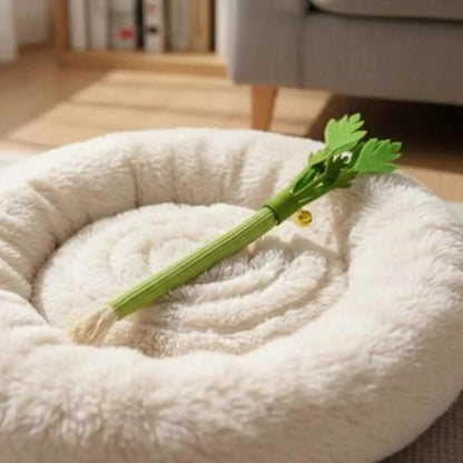 Bâton à mâcher pour chat vert avec feuilles et clochette dorée, posé sur un coussin